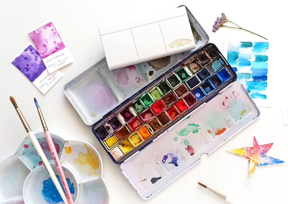capsa d'aquarel·les amb taques de colors i amb pinzells 