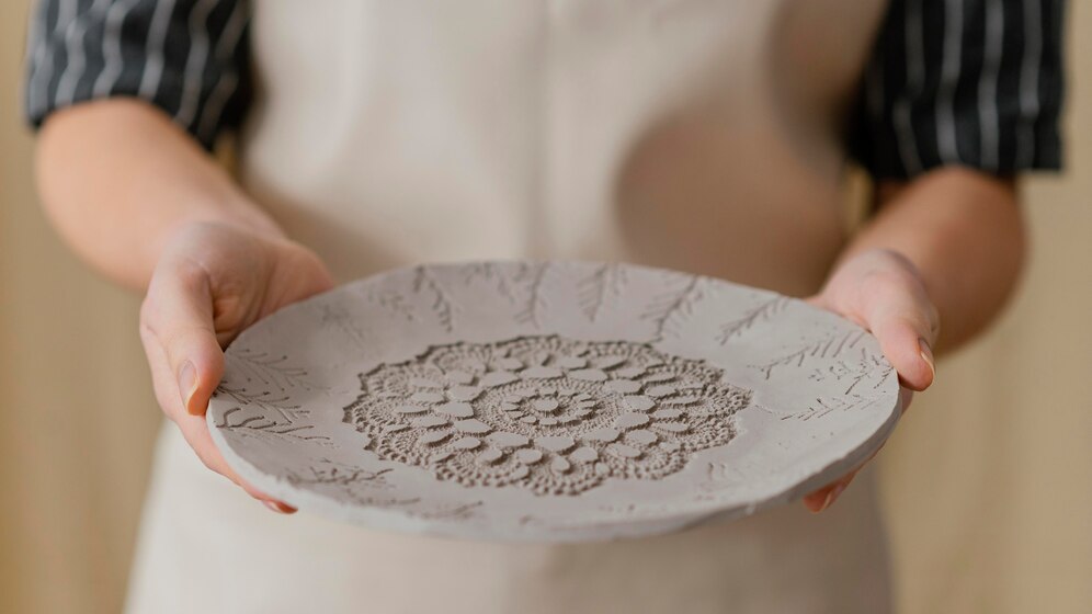 mans subjectant plat de ceràmica fresca amb un disseny grabat d'una mandala